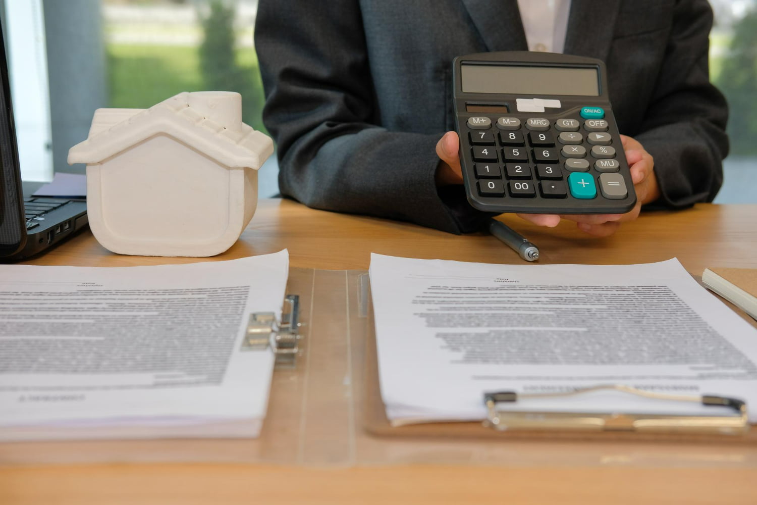 Homem segura calculadora para calcular taxa administrativa de consórcio, ao lado de maquete de casa