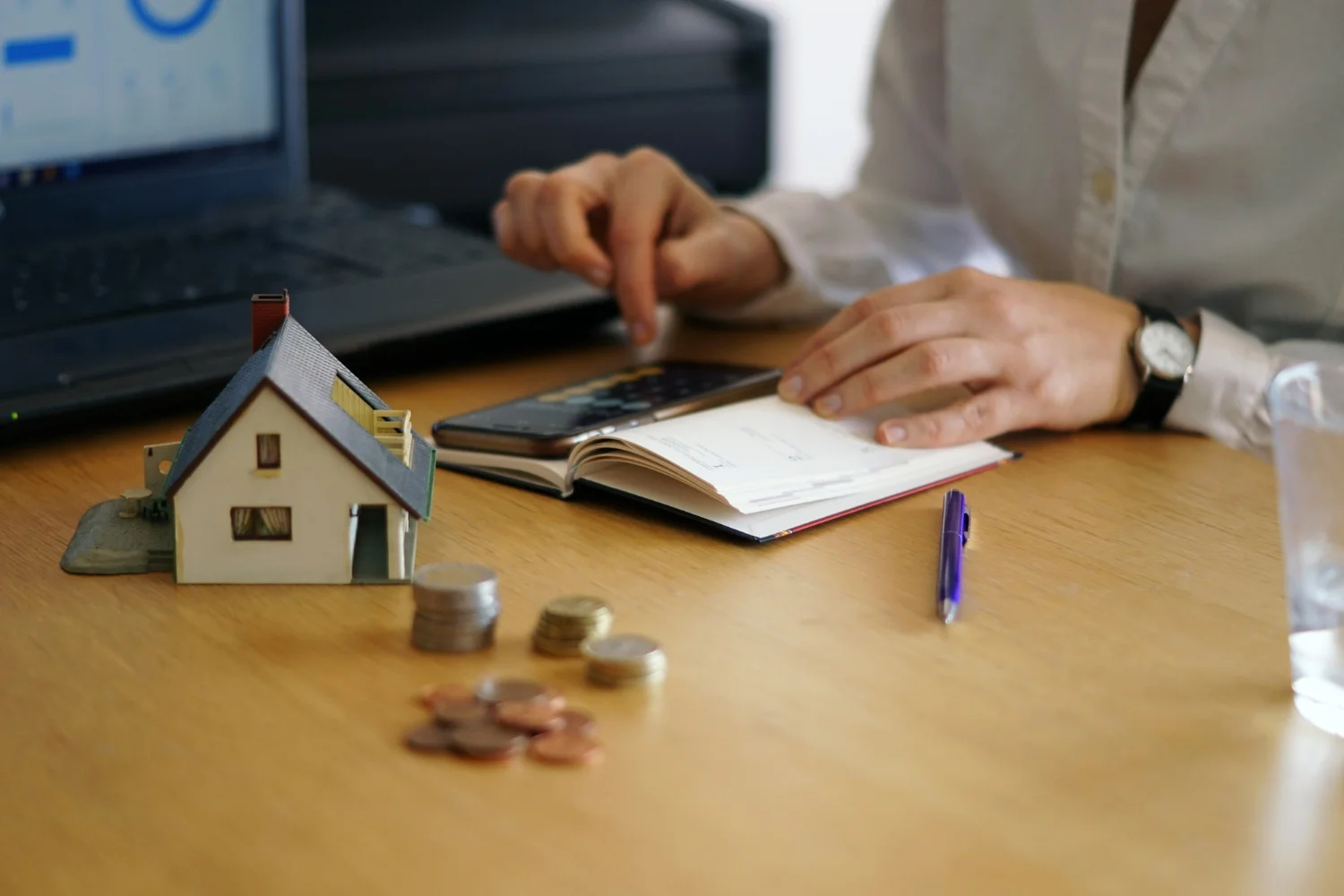 Pessoa calcula despesas ao lado de uma casa em miniatura para avaliar as vantagens do consórcio